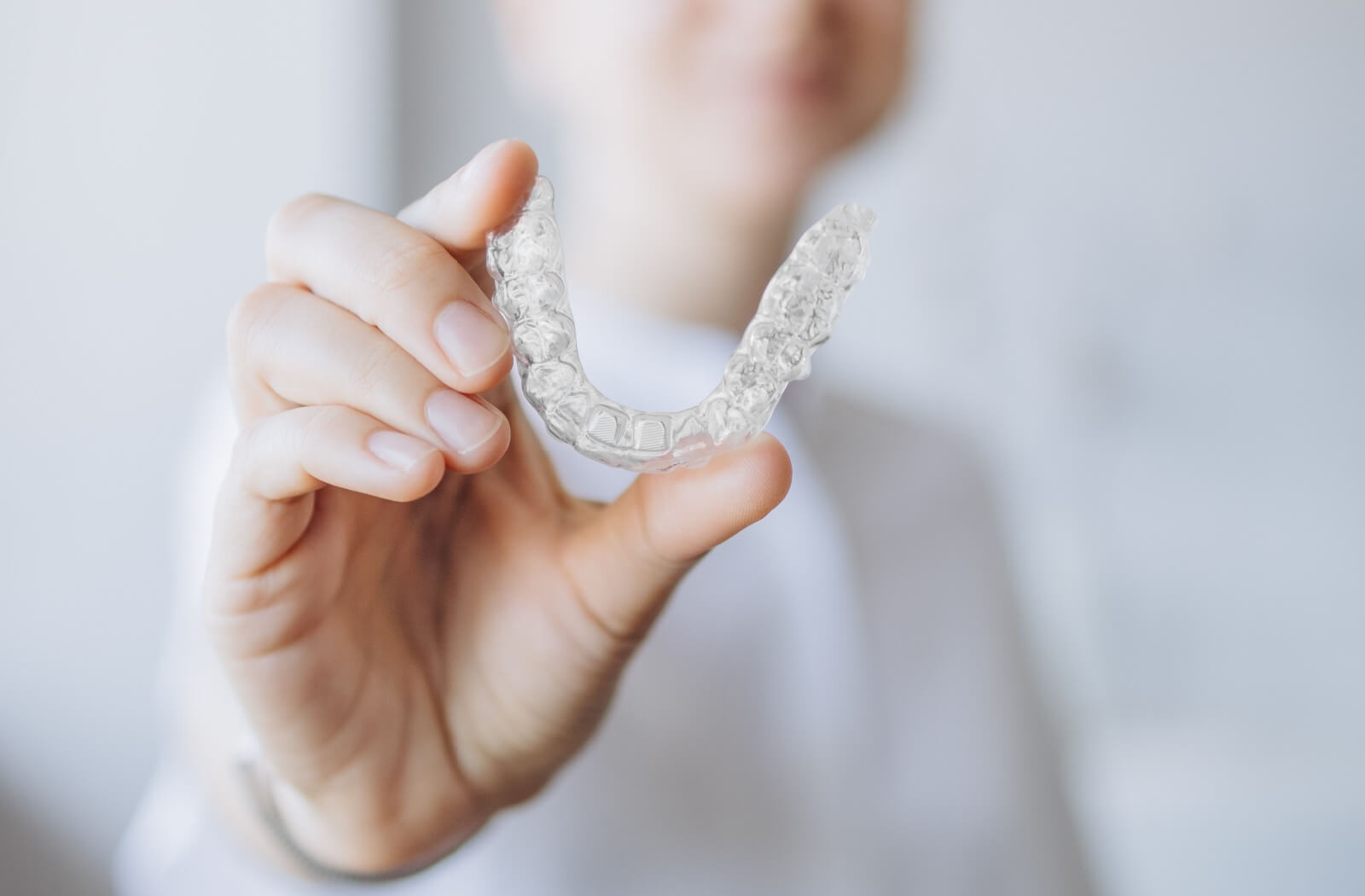Close-up of a dentist holding a clear Invisalign aligner into focus.