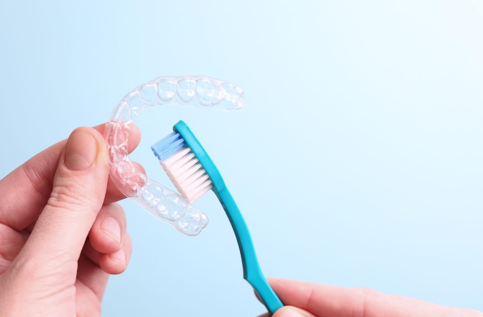 A person gently cleans their Invisalign aligner using a soft-bristle toothbrush.