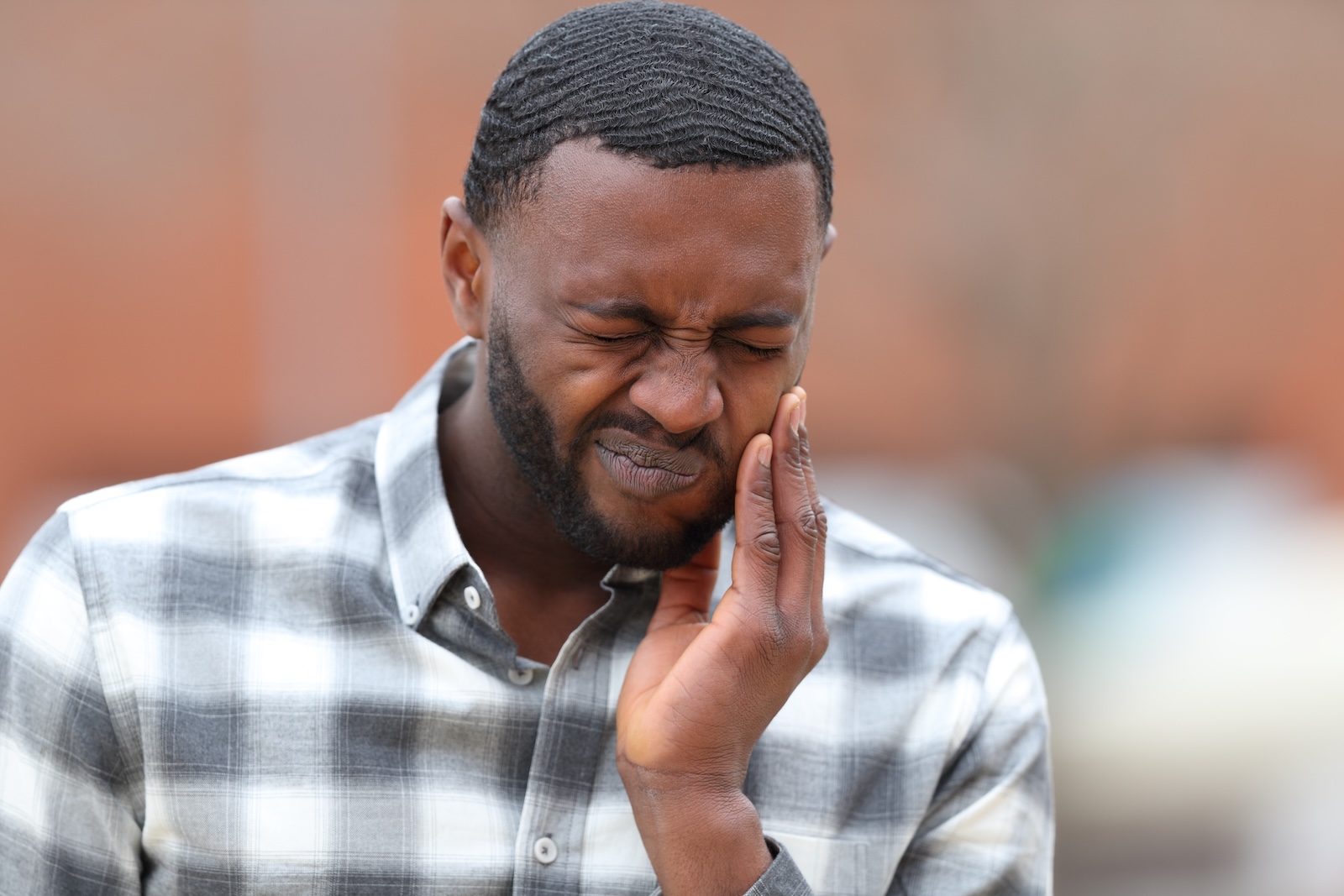 A man holds his hand to the left side of his jaw as he experiences severe jaw discomfort.